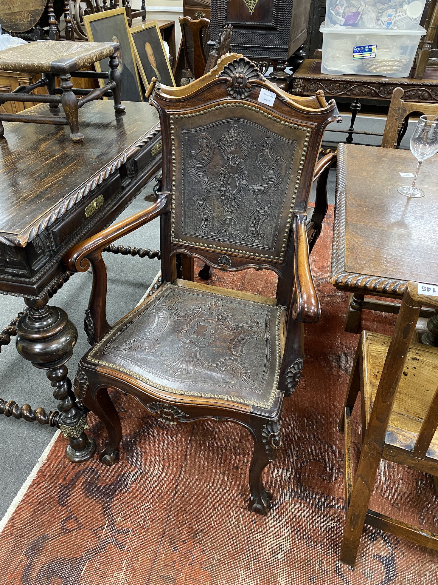 A pair of continental Spanish style carved elbow chairs with tooled leather backs and seats, width 62cms height 108cms.